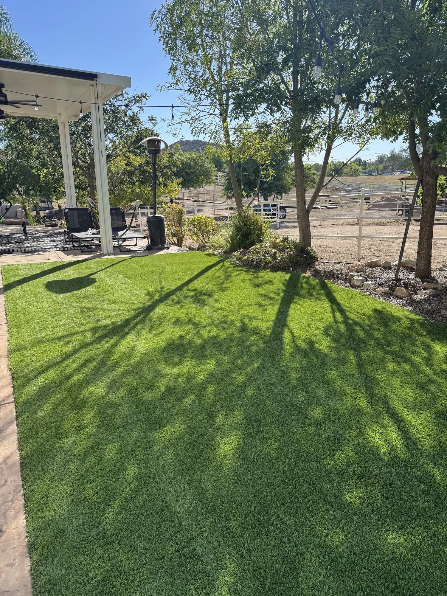Freshly cleaned backyard turf beside a covered patio, with ranch fencing and hills behind
